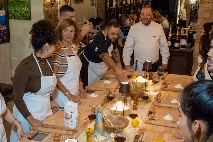 Chef guiding a group in a hands-on pasta and tiramisu cooking class with wine in Florence.