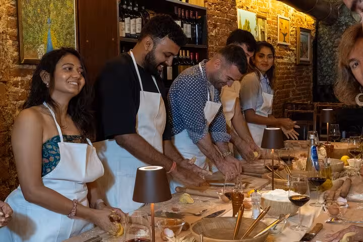 Participants rolling dough at a Florence pasta making class, surrounded by wine and cooking utensils.