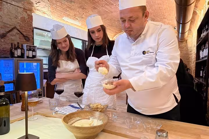 Chef demonstrates tiramisu preparation to engaged participants in Florence cooking class with unlimited wine.