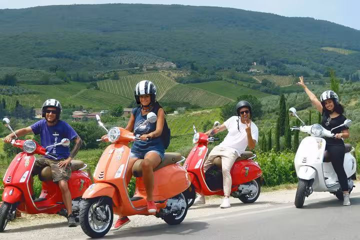 Group of tourists on Vespas enjoying a scenic ride through Tuscany's lush vineyards and rolling hills.