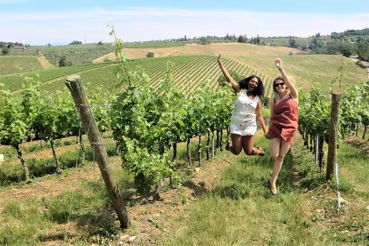 Two women joyfully jumping in a lush Tuscan vineyard during a scenic Vespa tour from Florence.