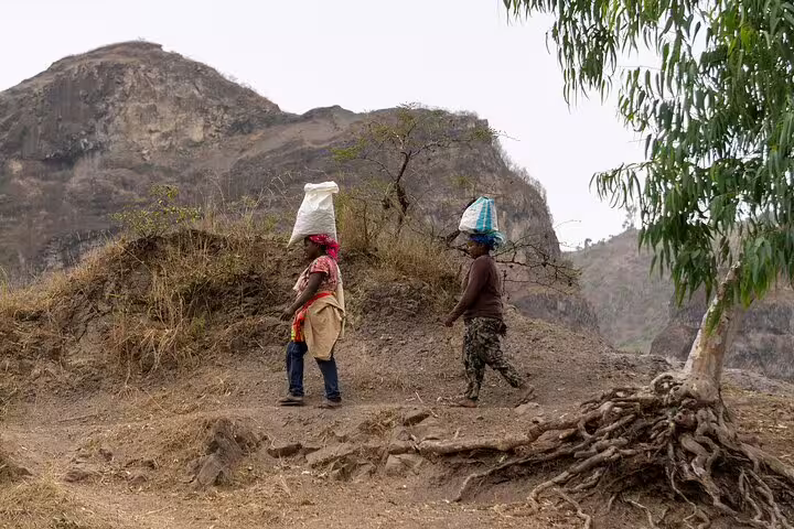 Two locals carrying bags on their heads along a scenic path on Fogo Island, highlighting cultural and natural landscapes.
