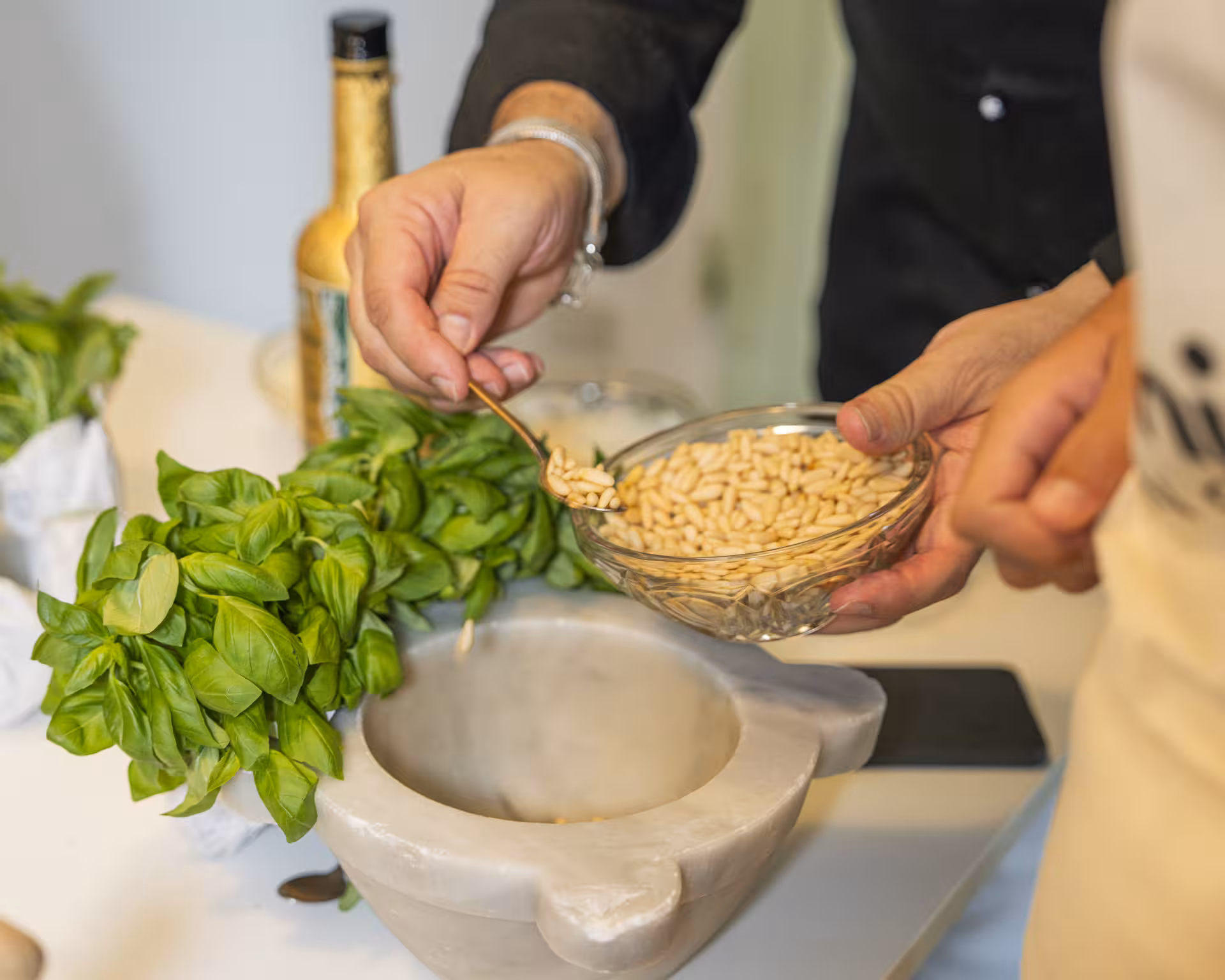 Hands preparing fresh pesto with basil and pine nuts in a marble mortar, highlighting the culinary experience in Liguria.