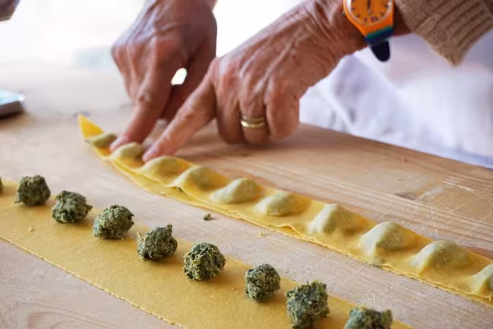 Hands crafting fresh ravioli with spinach filling on a wooden table in a Florence cooking class.