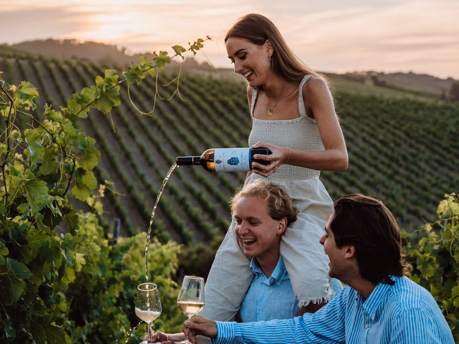 Joyful moment of friends enjoying wine tasting in a scenic Tuscan vineyard at sunset near Pisa, Italy.