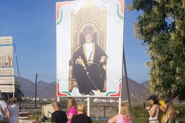 Tourists viewing royal portrait landmark with Hajar Mountains backdrop on Fujairah Khorfakkan sightseeing tour