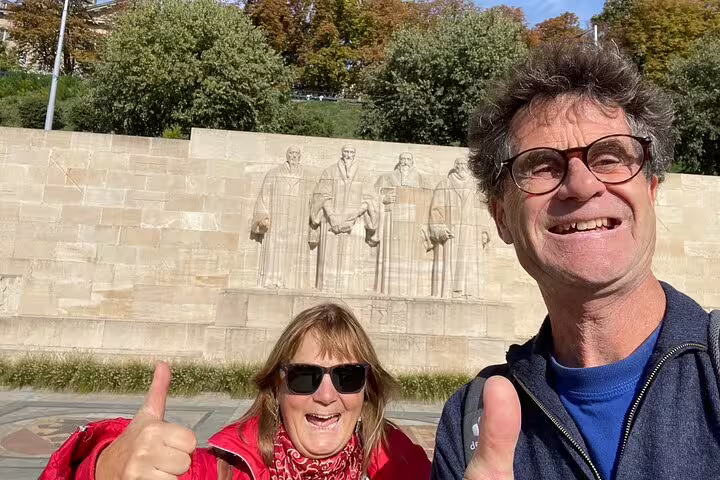 Couple smiling at the Reformation Wall on a Geneva scavenger hunt and city highlights walking tour in sunshine