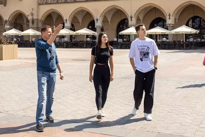 Tour guide explains historical sites to two tourists in a vibrant city square during the Ghetto and World War II Walking Tour.