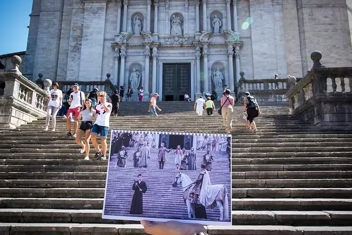 Tourists explore the iconic steps of Girona Cathedral with an image from a famous TV series in hand, capturing history.
