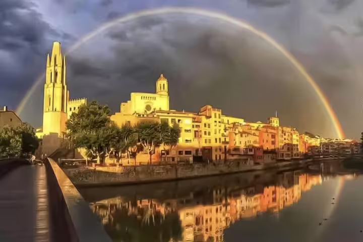 Scenic view of Girona's medieval architecture under a dramatic sky with a rainbow, perfect for a private tour.