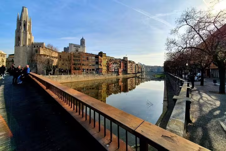 Scenic view of Girona's Onyar River with historic buildings and Cathedral reflecting in the calm waters, perfect for a cultural tour.