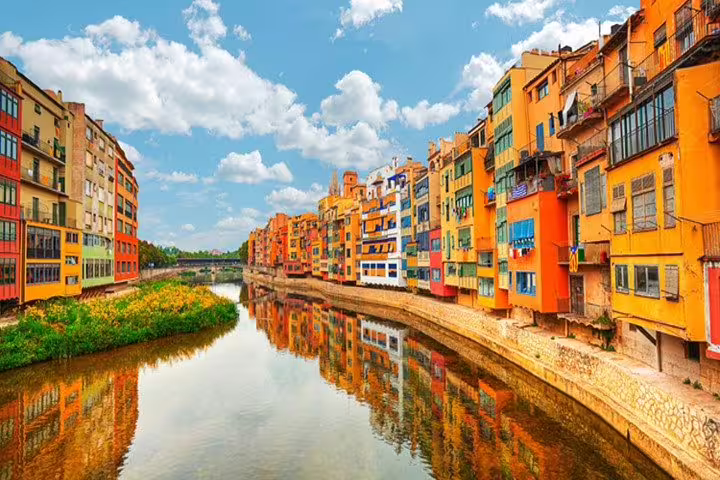 Vibrant houses reflecting in the Onyar River under a blue sky, a picturesque view on the Girona Tour.