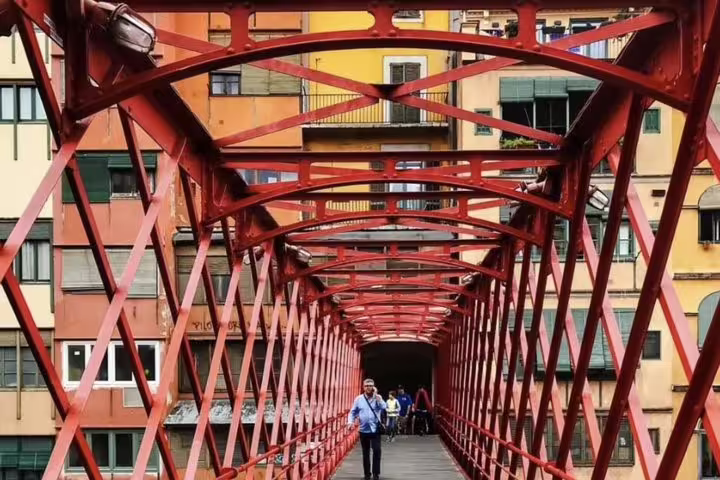 Vibrant red pedestrian bridge in Girona with colorful historic buildings, part of a medieval gems private tour.