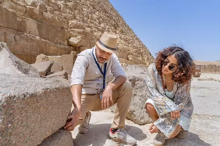 Tour guide and traveler examining stonework near the Great Pyramid of Giza on Sphinx and Saqqara day tour