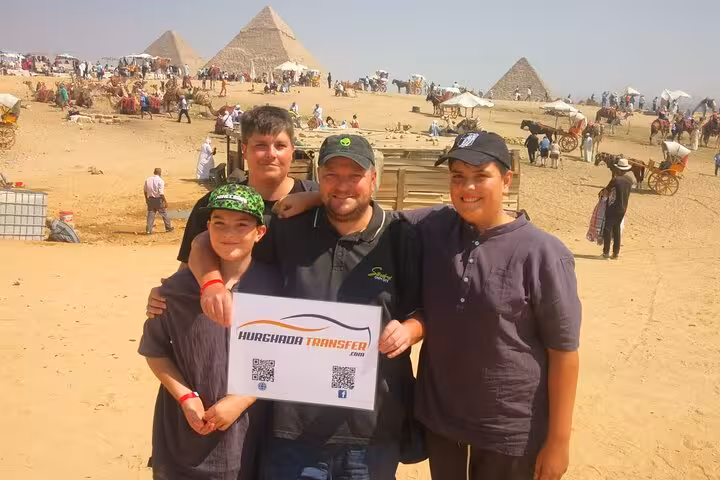 Tour guests posing at Giza Pyramids on a full day Cairo excursion, with desert panorama and camels behind