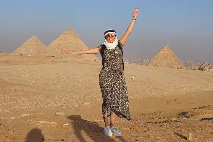 Traveler posing in Giza desert with pyramids on private tour including entry tickets, lunch, camel and quad rides