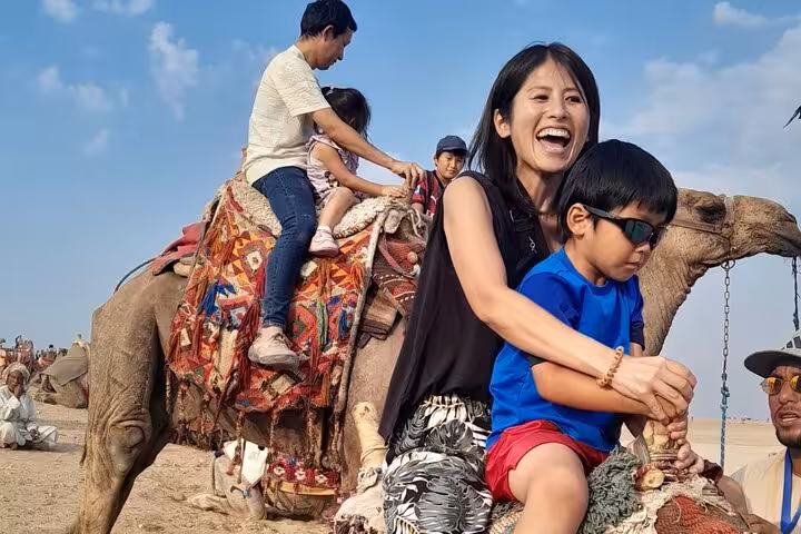 Family enjoying a camel ride at Giza Pyramids on a private tour with quad biking, entry tickets and lunch