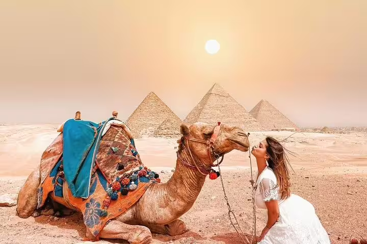 Private camel tour at Giza Pyramids at sunset, traveler by saddled camel with pyramids behind