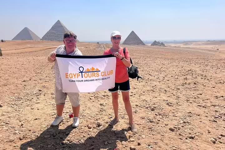 Couple holding tour banner at Giza Plateau with pyramids behind on private Cairo day trip from Memphis