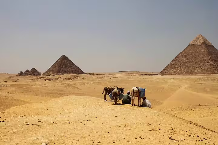 Camel handlers resting in the Giza desert with pyramids in view, part of a horse carriage half-day tour