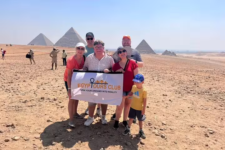 Private Giza Pyramids tour group photo in Cairo desert with Great Pyramid and tour banner in foreground