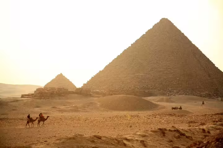 Sunset view of Giza Pyramids with camel riders on a private guided tour with hotel transfers and entry tickets