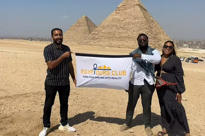 Travelers pose with guide at Giza Pyramids holding tour banner on a half-day pyramids tour in Cairo, Egypt