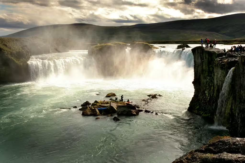 Godafoss waterfall with mist rising and tourists viewing from rocky cliffs near Akureyri Iceland
