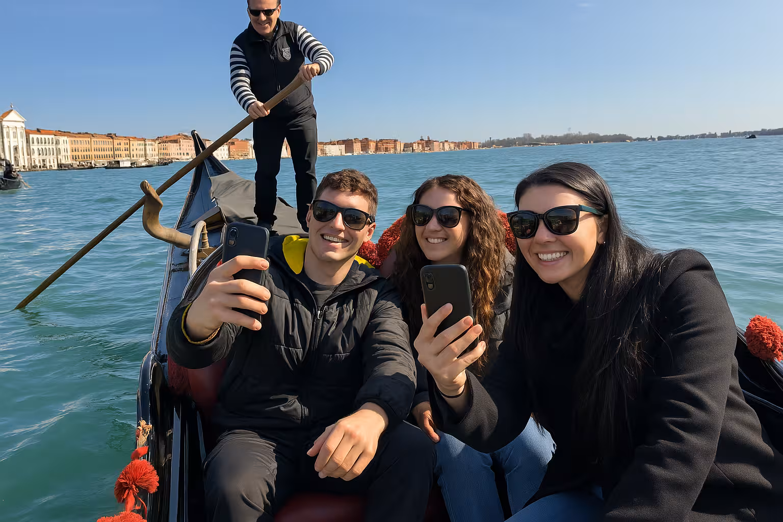 Group enjoying a shared gondola ride on St. Mark's Basin, capturing selfies with a scenic Venetian backdrop.