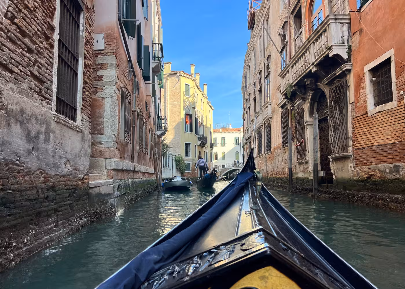 Gondola gliding through Venice's narrow canal, showcasing historic architecture under clear blue skies.