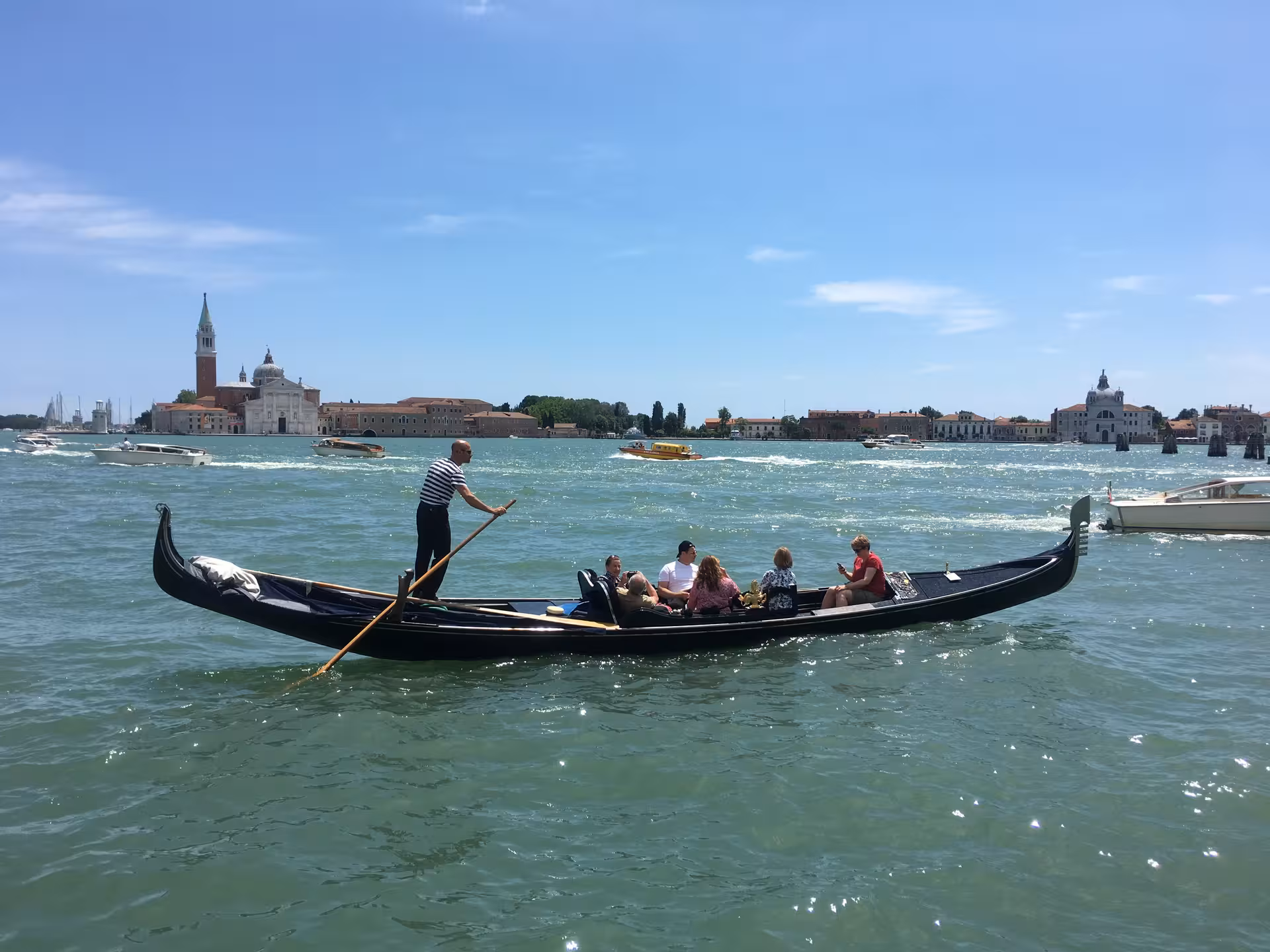 Gondolier navigating with tourists on Venice's Grand Canal, picturesque islands in the background.