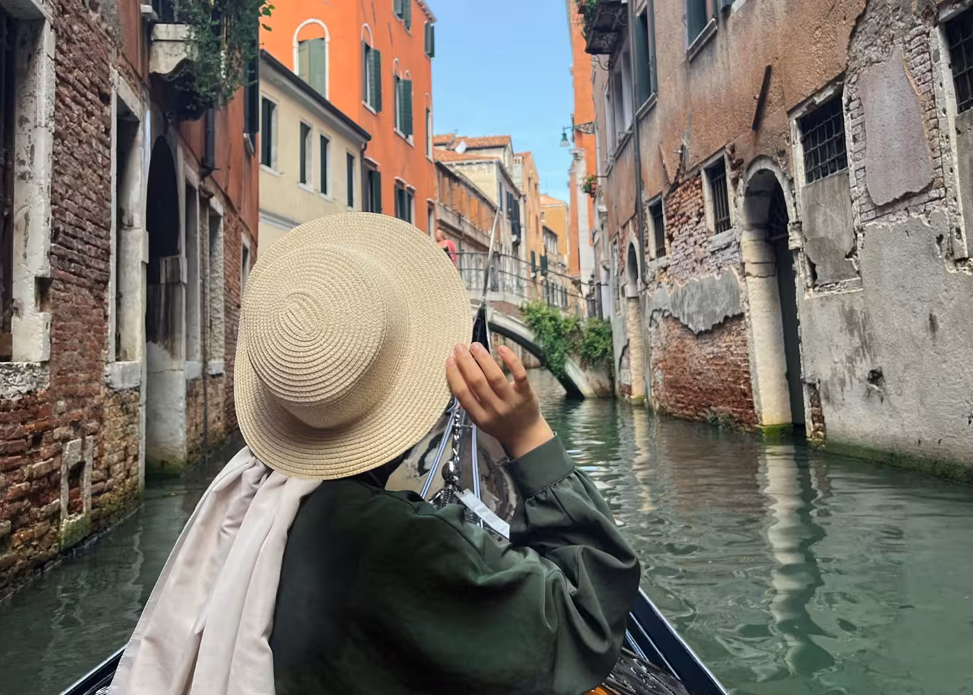 Traveler in a straw hat explores narrow Venetian canals during a charming gondola ride with app-guided commentary.