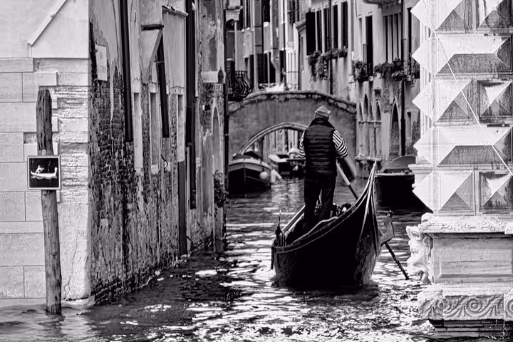 A gondolier navigates a narrow Venetian canal in black and white, showcasing the charm of a gondola ride tour.