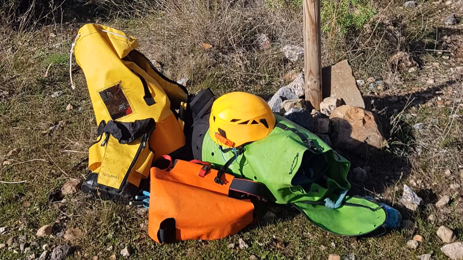 Colorful dry canyoning gear including helmet and bags on grassy terrain, ready for Gonnesa's Monte San Giovanni tour.
