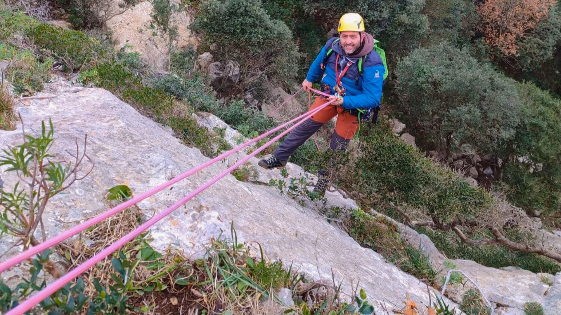 Smiling climber rappelling down a steep rock face with ropes on Monte San Giovanni, showcasing dry canyoning adventure.