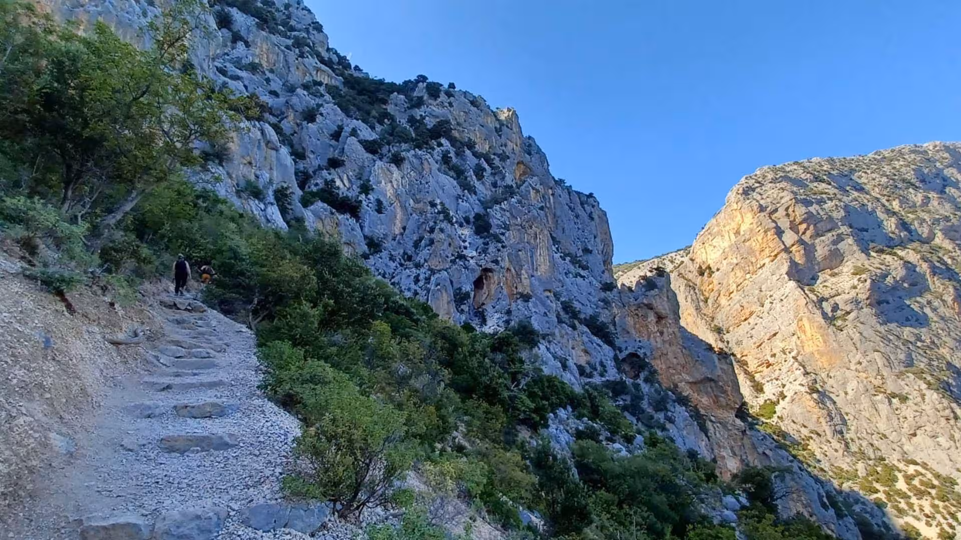 Hikers exploring the rugged paths of Gorropu Canyon under a clear blue sky in Sardinia.