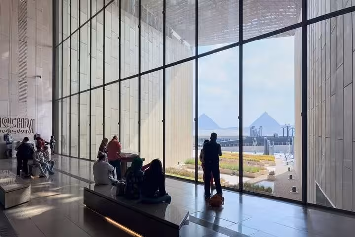 Grand Egyptian Museum glass atrium with visitors and panoramic view of Giza Pyramids on a guided tour