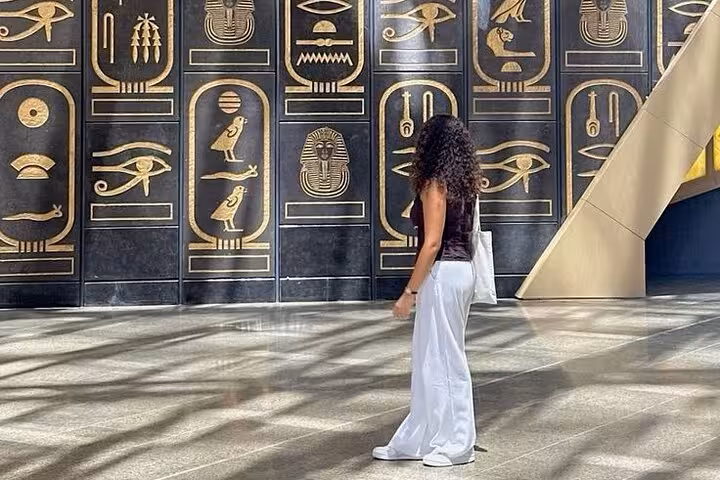 Visitor at Grand Egyptian Museum Giza beside gold hieroglyph wall on GEM, Pyramids and Sphinx tour