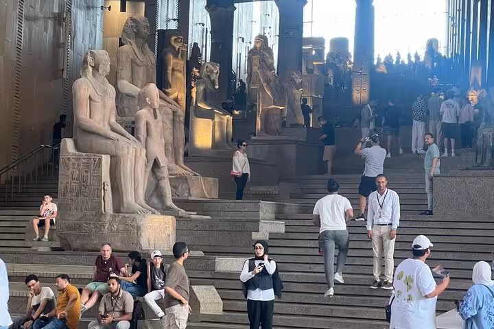 Grand Egyptian Museum private guided tour Cairo, visitors on steps beside ancient statues in the grand hall
