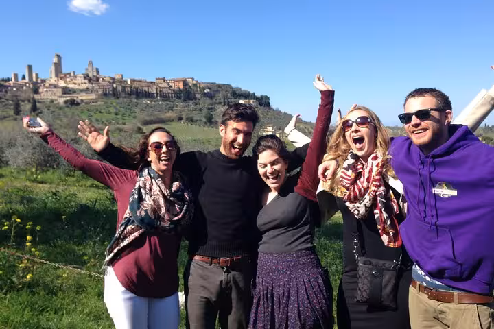 Excited group posing with San Gimignano skyline in the background, part of Tuscany wine tour from Florence.