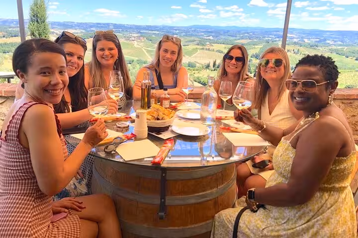 Group of friends savoring wine and snacks at a Tuscan winery with panoramic views of rolling hills.