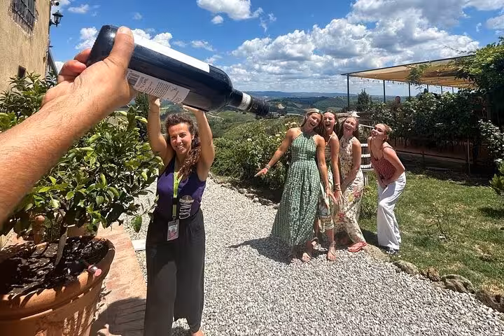 Group of friends laughing as a large wine bottle is playfully poured over them at a Tuscan winery.