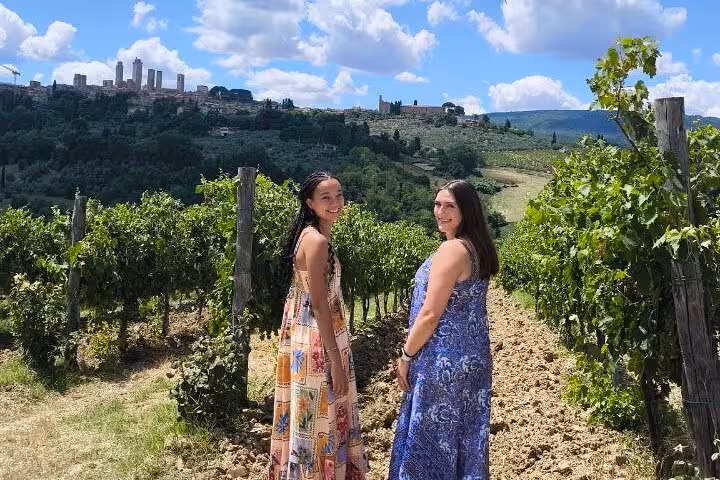 Two women in colorful dresses walking through a vineyard in Tuscany with San Gimignano in the background.