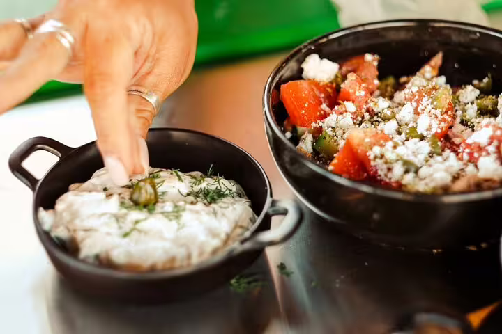 Adding dill to tzatziki beside Greek salad in Athens cooking class, classic meze before rooftop dinner with views