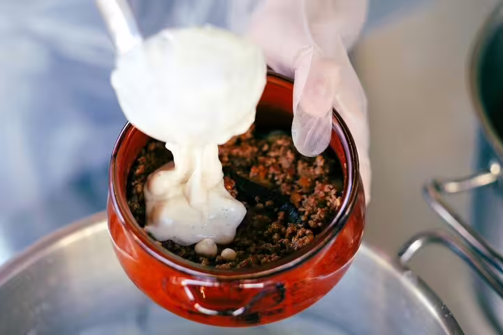 Close-up of yogurt sauce poured over spiced filling in clay pot at Athens Greek cooking class experience