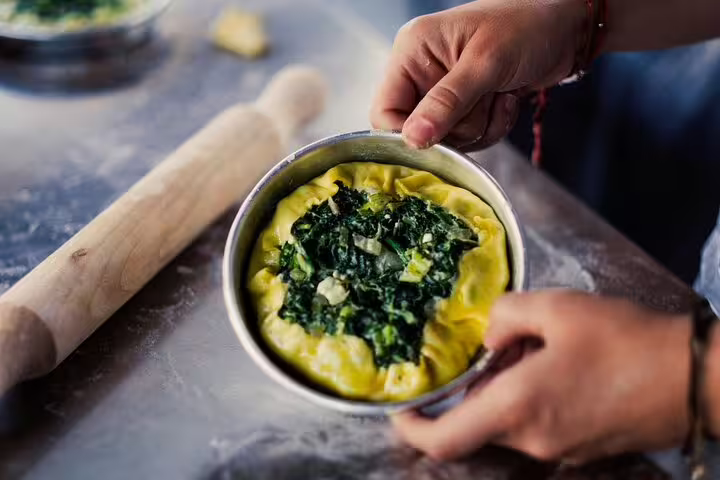 Hands shaping Greek spinach pie in pan during Athens cooking class, traditional filo prep for rooftop dinner