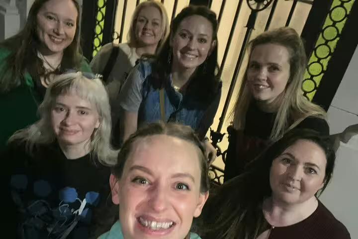 Group of seven women smiling together at night during haunted walking tour in Bucharest Old Town