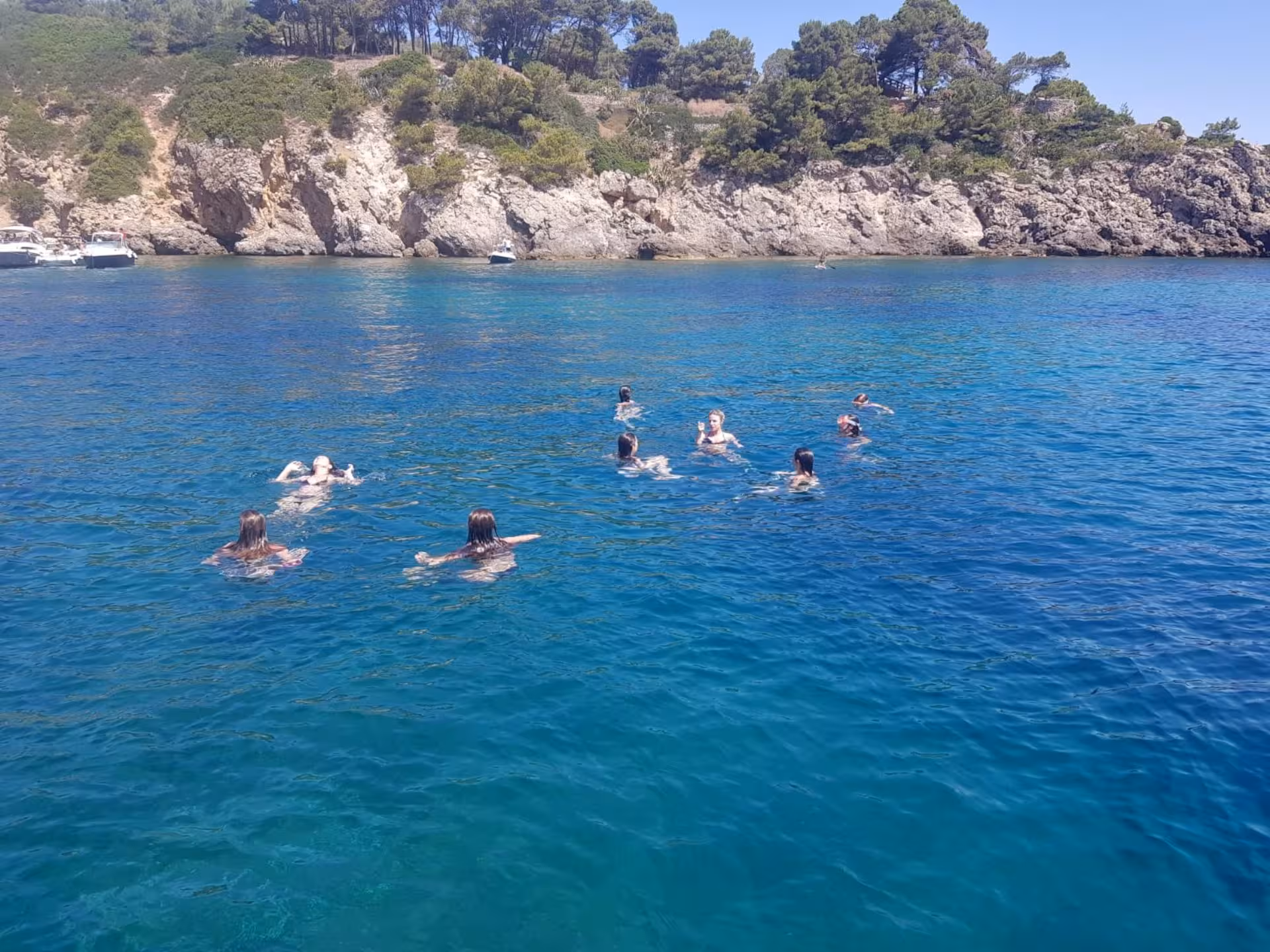 Group of people swimming in the clear blue waters of the Gulf of Alghero near rocky cliffs.