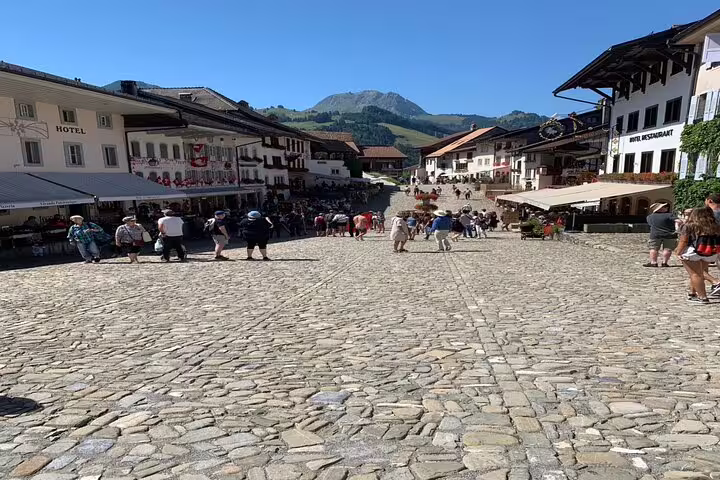 Charming cobblestone street in Gruyères village, surrounded by traditional Swiss architecture and scenic mountain views.