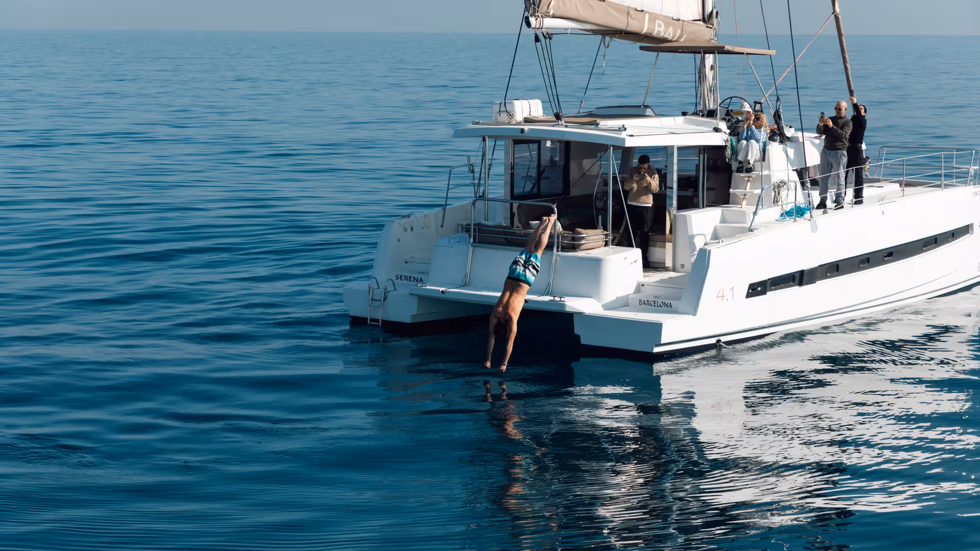 Guest diving from Bali 4.2 catamaran on a 4-hour private luxury Barcelona sailing charter in calm sea